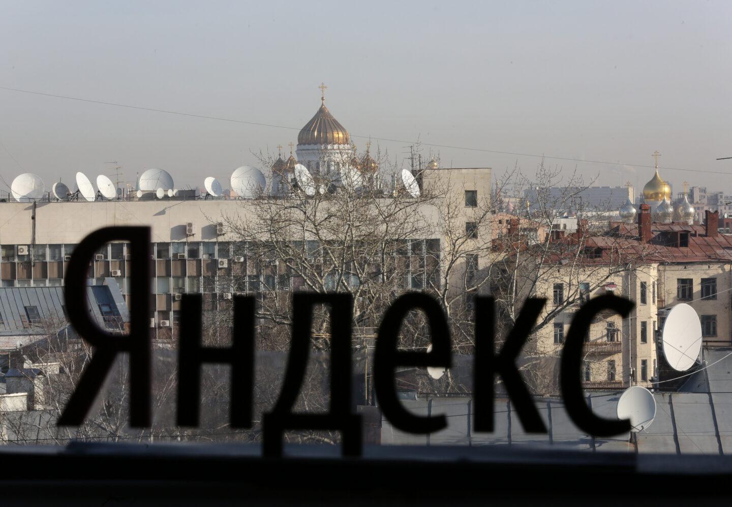 Widok z okna siedziby firmy Yandex. Na szybie widnieje rosyjska nazwa przedsiębiorstwa. Na horyzoncie widać dachy z licznymi antenami satelitarnymi oraz złote kopuły moskiewskich cerkwi.
